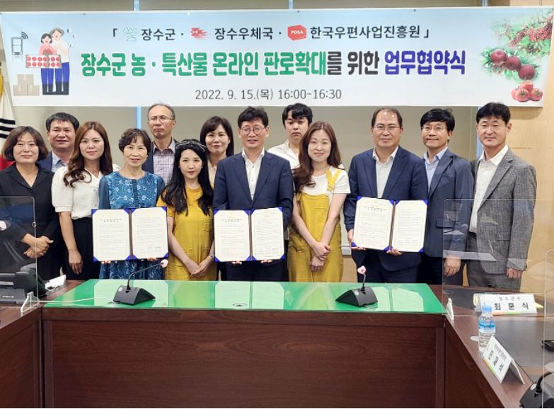 장구순, 장수우체국, 한국우편사업진흥원 / 장수군 농 특산물 온라인 판로 확대를 위한 업무 협약식 / 현수막 아래에서 단체로 사진을 찍는 모습