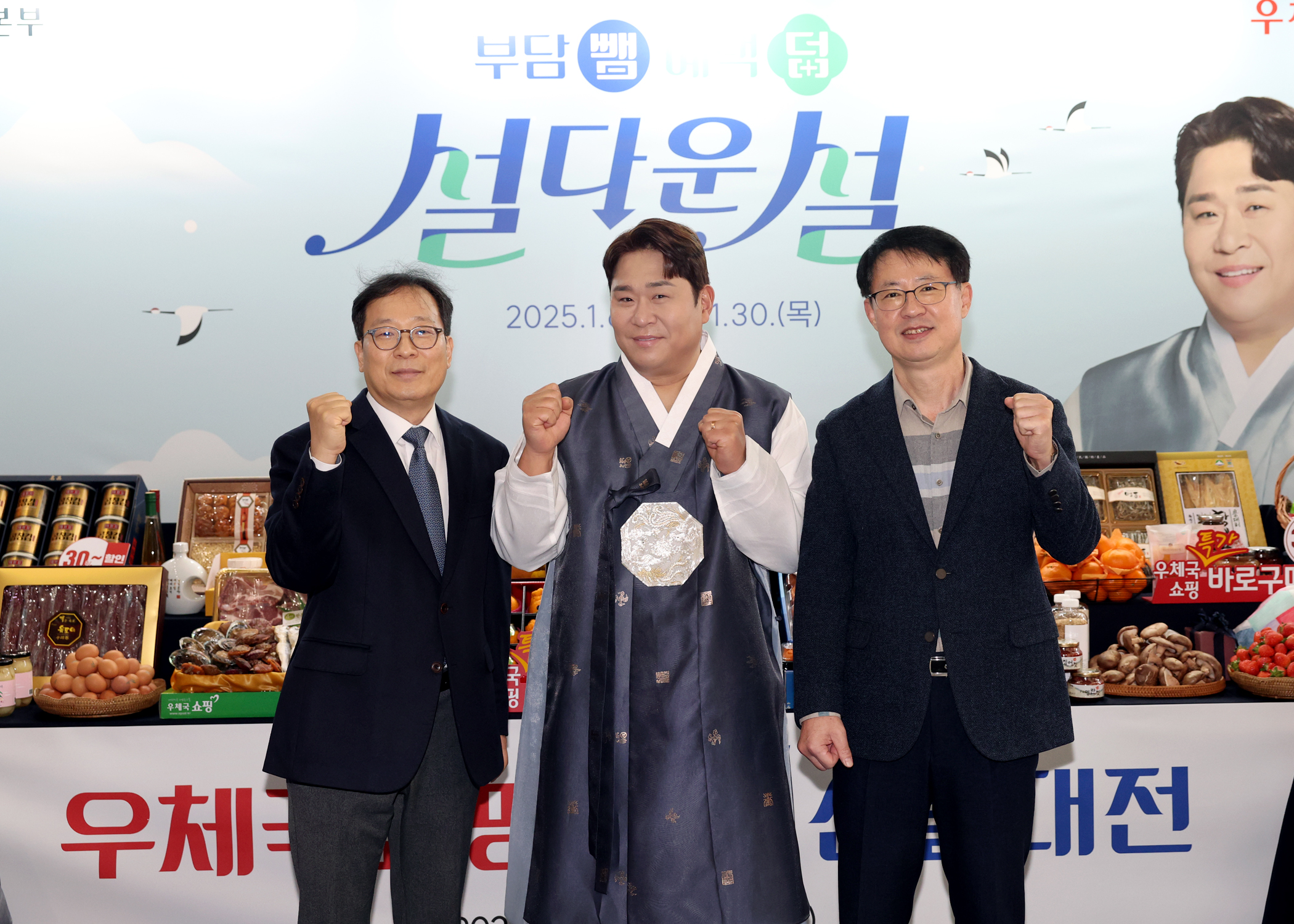 2025년 설 선물대전 포스터 앞에서 선물세트를 등지고 한국우편사업진흥원장과 포스터 모델, 관계자가 포즈를 취하고 기념사진을 찍는 모습