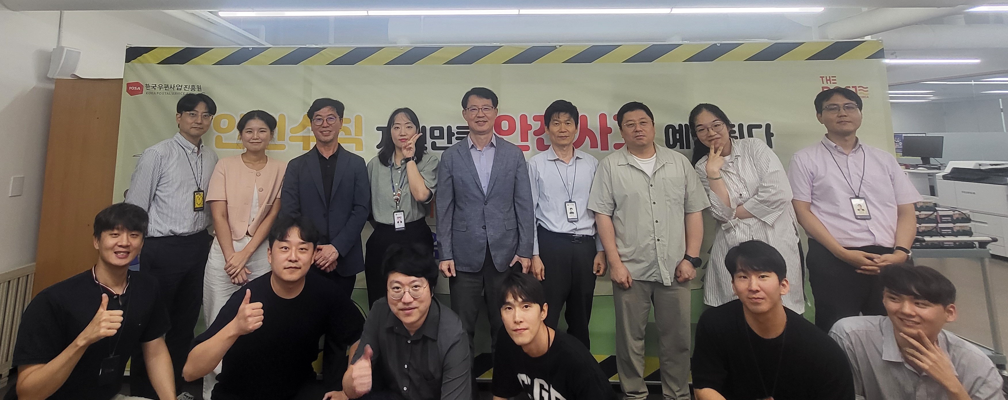 POSA 안전 캠페인 배너 앞에서 모여 기념촬영 중인 직원 단체사진. 앞줄 일부는 앉거나 손가락으로 포즈를 취한 모습