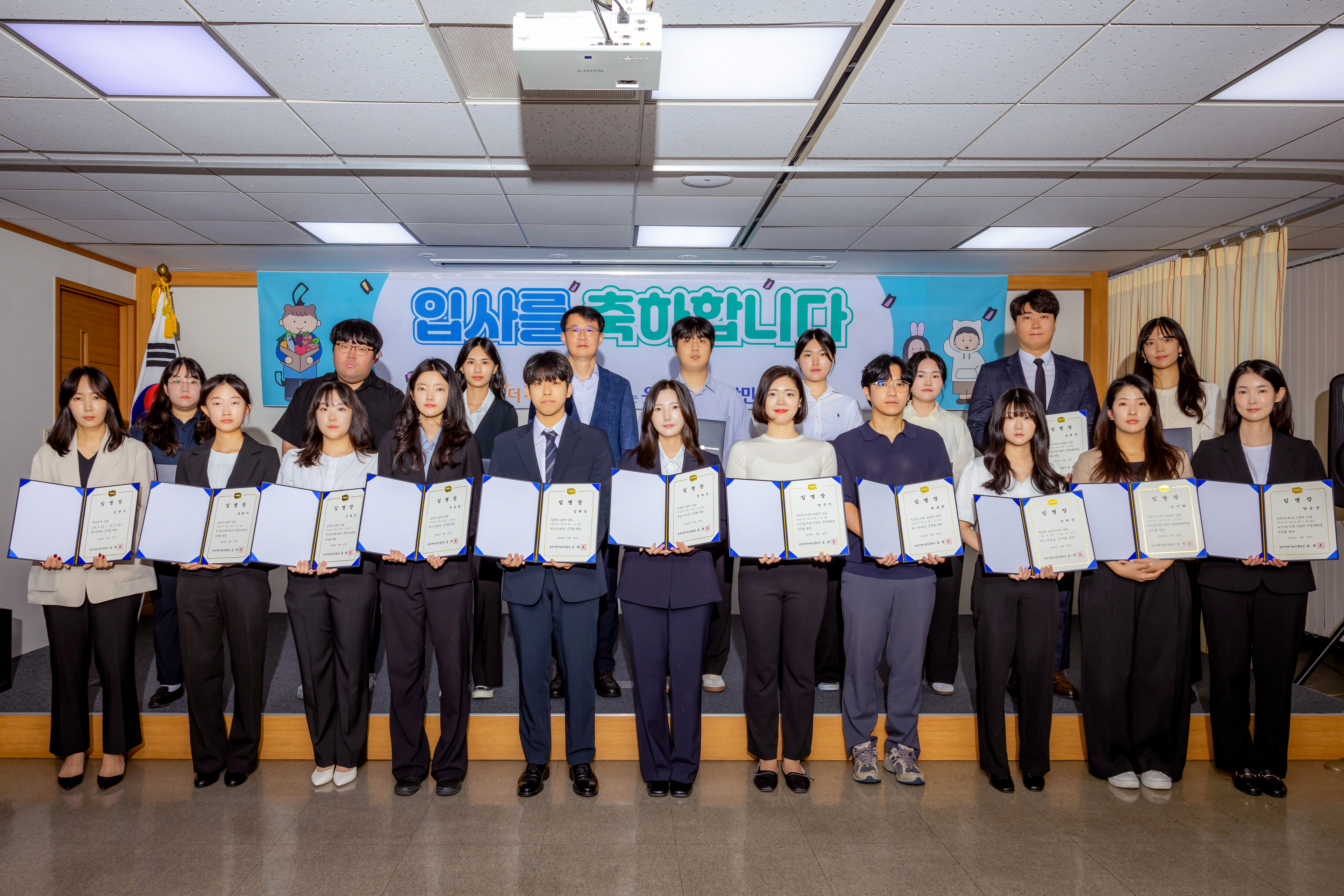 신입직원 임명장을 펼쳐서 기념촬영 중인 직원 단체사진