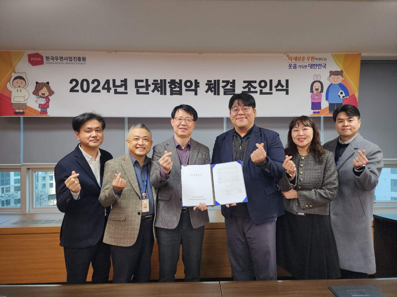 2024년 단체협약 체결 조인식 현수막 앞에서 체결협약서를 들고 6명이 단체사진 찍는 모습