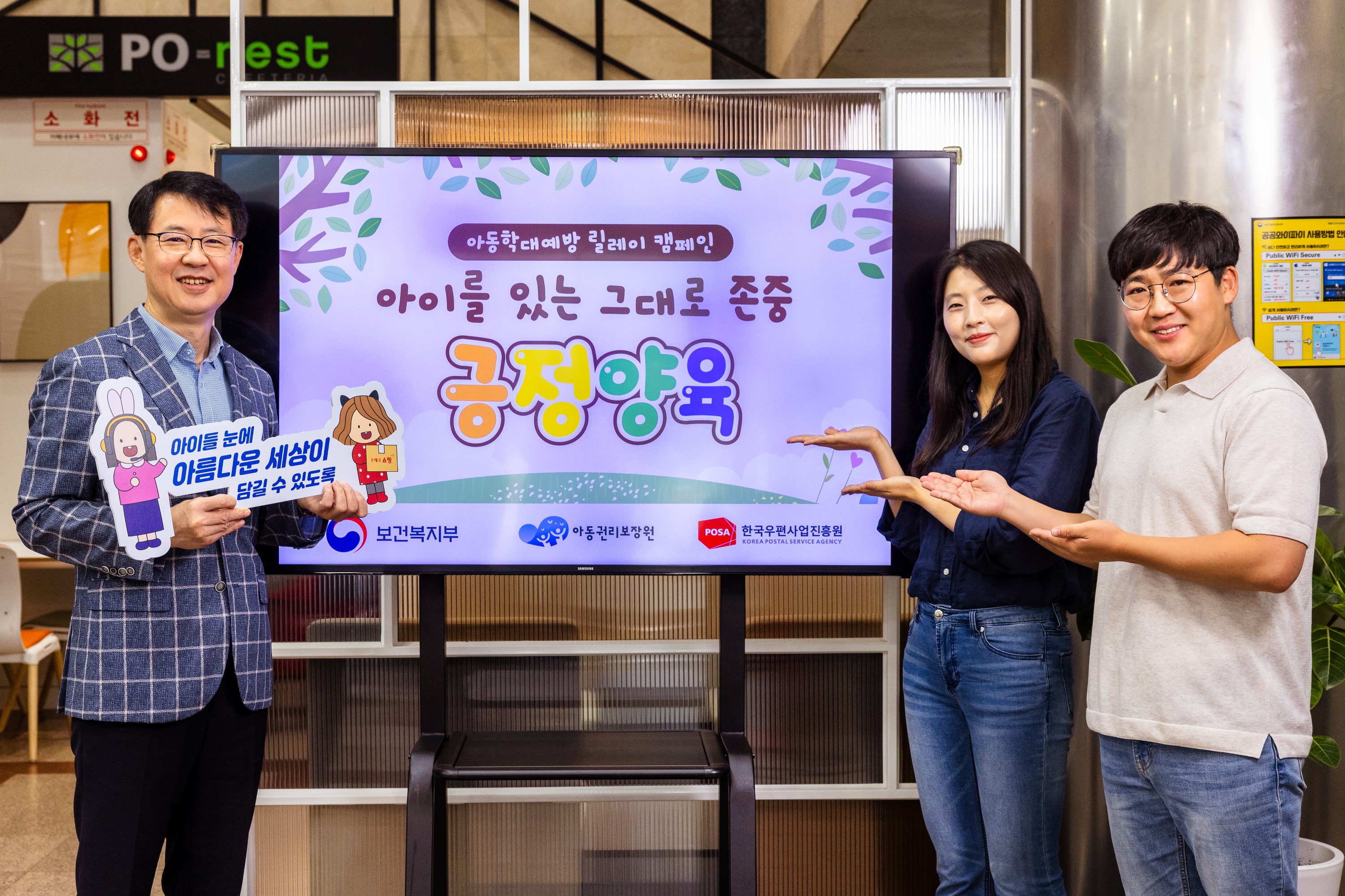 아동학대예방 릴레이’ 캠페인 홍보 화면 앞에서 세 명의 성인이 캠페인을 소개하며 포즈를 취하고 있는 모습
