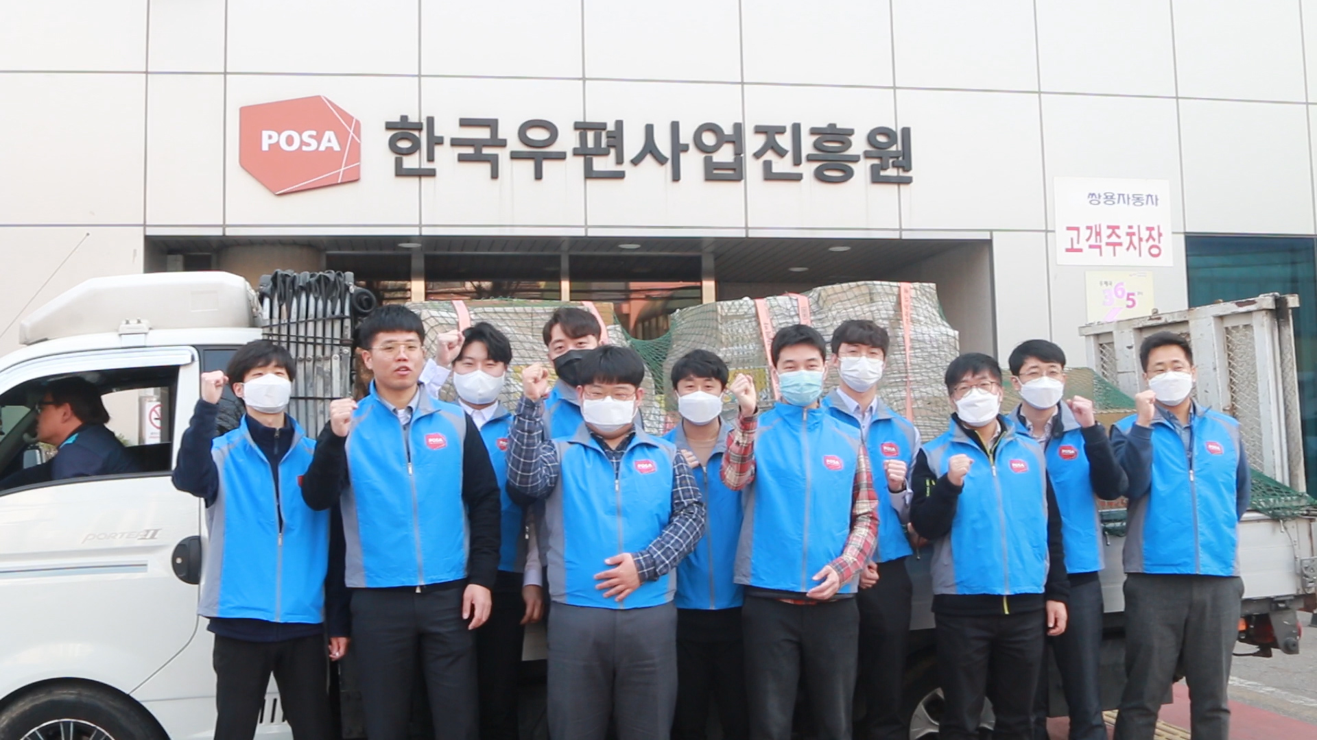 POSA 한국우편사업진흥원 앞에서 마스크를 끼고 화이팅을 하며 사진을 찍고 있습니다.한국우편사업진흥원은 코로나19 장기화로 인해 어려움을 겪고 있는 복지사각지대 취약계층,대구·경북지역 중소상공인과 지역 주민을 위한 지원 활동을 강화하였습니다.